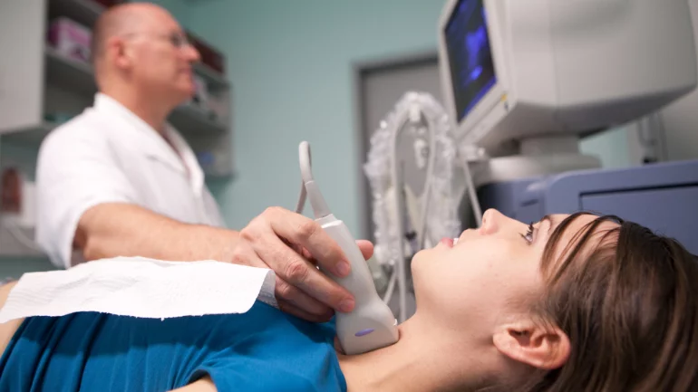 Ein Arzt untersucht die Schilddrüse einer jungen Frau per Ultraschall.