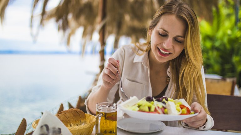 Eine junge Frau isst in einem Restaurant am Meer einen Salat