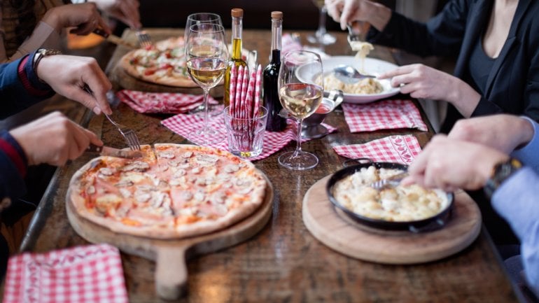 Man sieht einen Tisch in einem italienischen Restaurant, auf dem Pizza- und Pasta-Gerichte stehen.