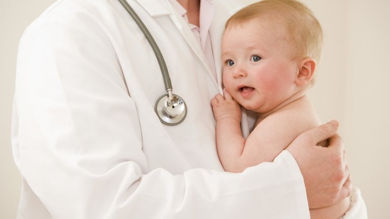 Das Bild zeigt ein Baby auf dem Arm eines Arztes.