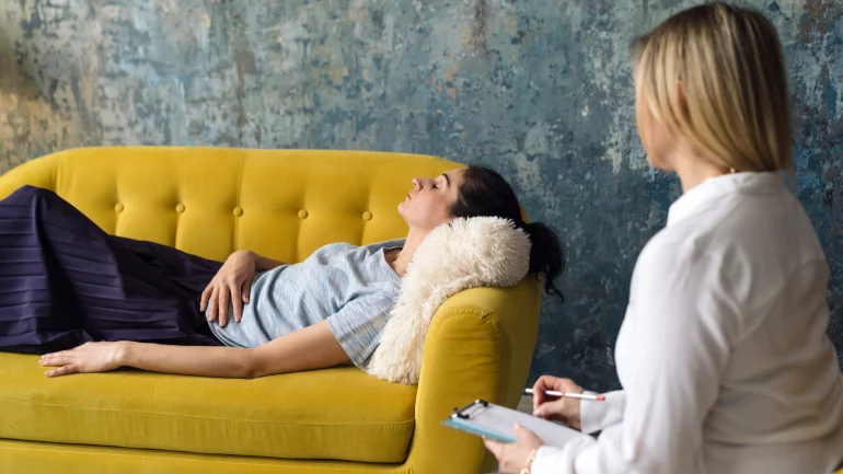 Frau liegt unter Hypnose auf Couch neben der Therapeutin.