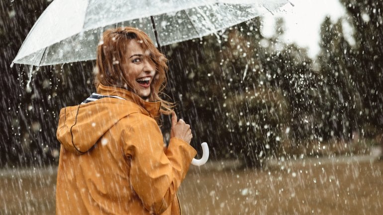 Eine Frau geht bei regnerischem Wetter mit Schirm spazieren und lacht