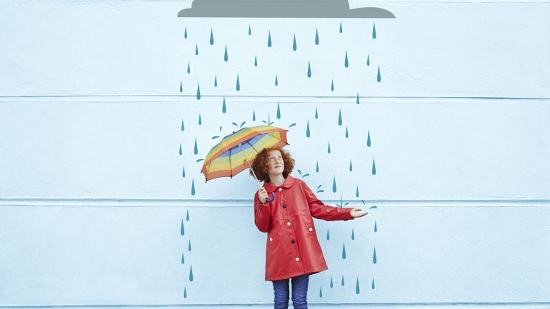 Eine Frau mit Schirm steht vor einer Wand, auf der Regen gemalt ist