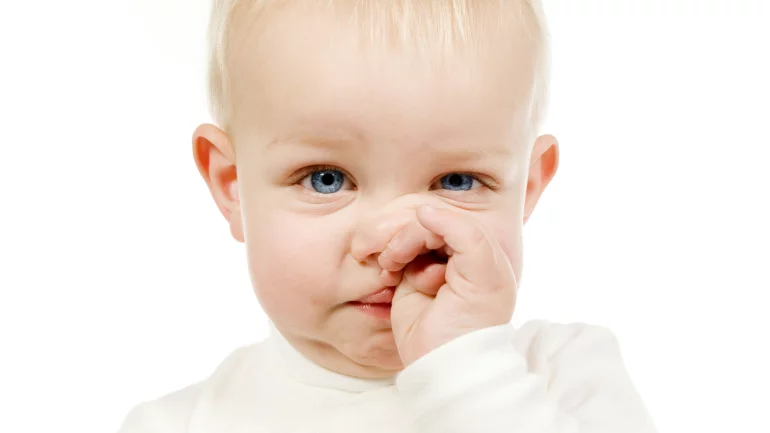Das Bild zeigt ein Kleinkind, das sich an die Nase greift.