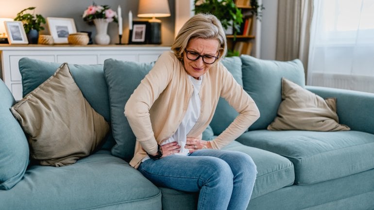 Interstitielle Zystitis: Frau hat Unterleibsschmerzen und sitzt auf einem Sofa