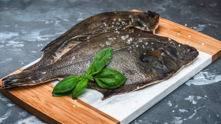 Jodhaltige Speisen: Roher Fischflunder mit Salz und Basilikum auf einer Küchentafel.