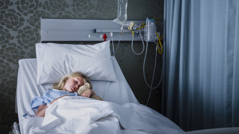 Ein Mädchen liegt mit ihrem Teddy in einem Krankenhausbett