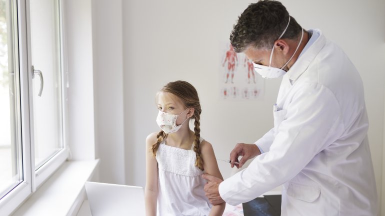 Ein Mädchen mit Maske wird von einem Arzt geimpft