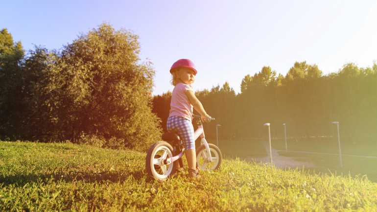 Ein kleines Mädchen mit Helm auf einem Laufrad.