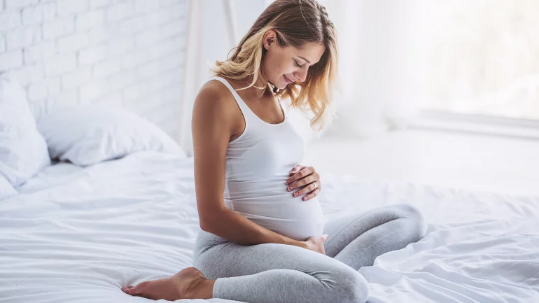 Eine schwangere Frau sitzt auf ihrem Bett und hält ihren Bauch