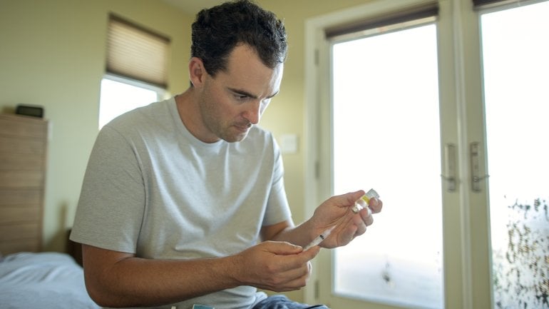 Mann mit Klinefelter-Syndrom sitzt auf seinem Bett und bereitet eine Spritze mit Testosteron vor