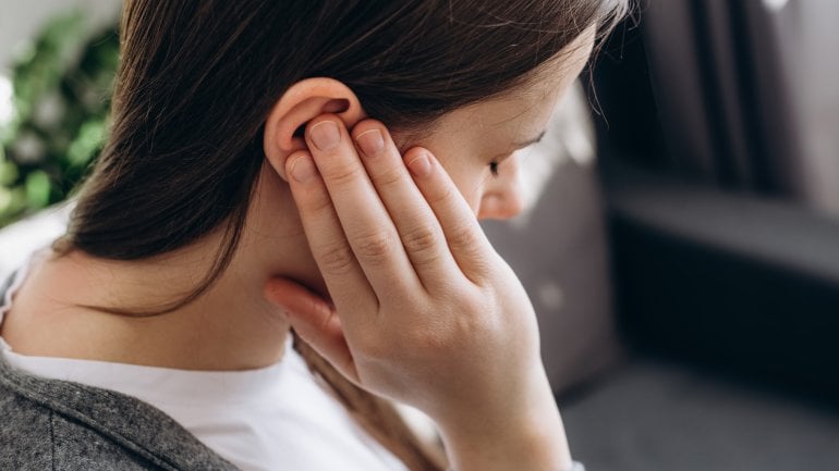 Eine junge Frau fasst sich an ihr Ohr, in dem sie ein Knacken wahrnimmt