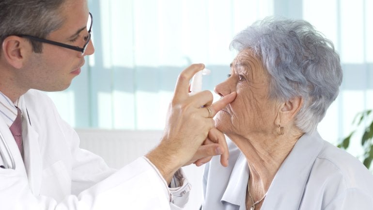 Ein Arzt betrachtet eine Stelle unterhalb des Auges bei einer älteren Frau.