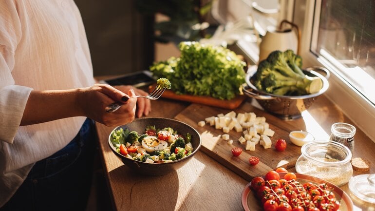Longevity-Ernährung: Tisch mit verschiedenen Gemüsen und eine gesunde Bowl von der eine Frau isst