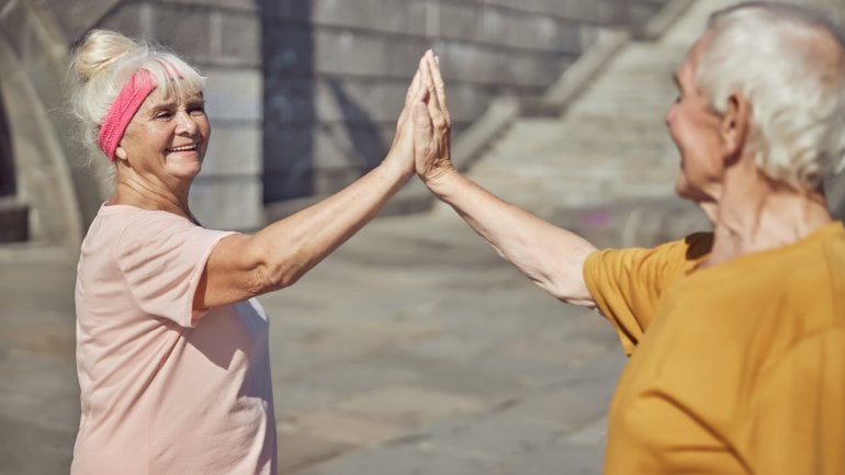 Zwei ältere Personen klatschen sich nach dem Sport im Freien ab.