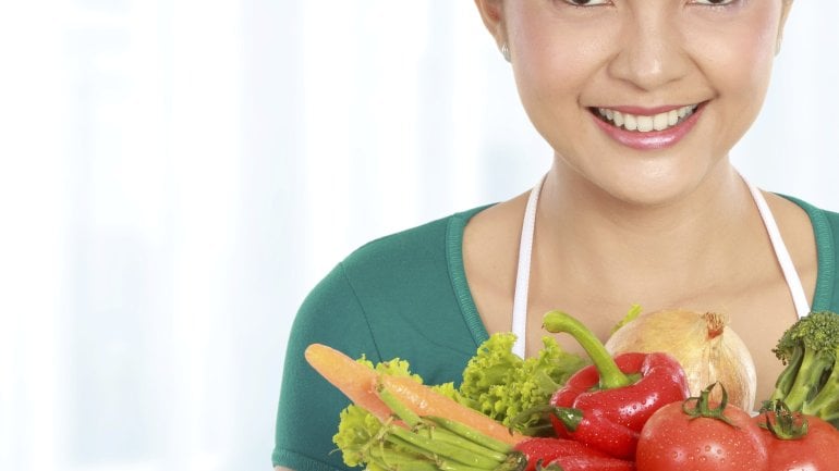 Das Bild zeigt eine Frau, die einen Teller mit Gemüse hält.