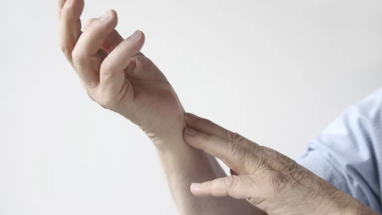Das Bild zeigt eine Person, die ihr schmerzendes Handgelenk hält.