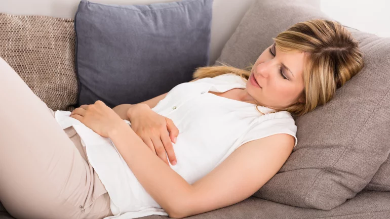 Eine Frau liegt mit Magenschmerzen auf dem Sofa