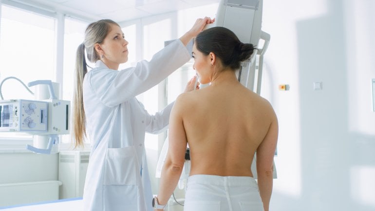 Ärztin platziert Patientin für Mammographie am Gerät.