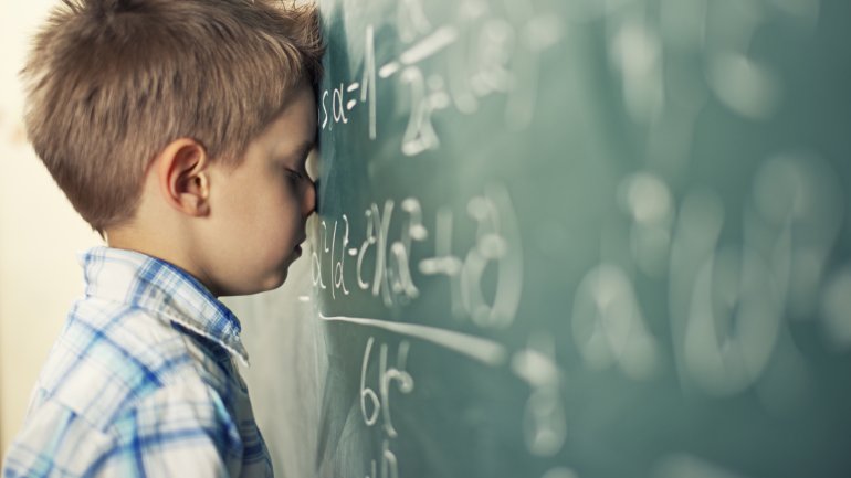 Das Bild zeigt einen kleinen Jungen, der an der Tafel steht und eine Matheaufgabe löst.
