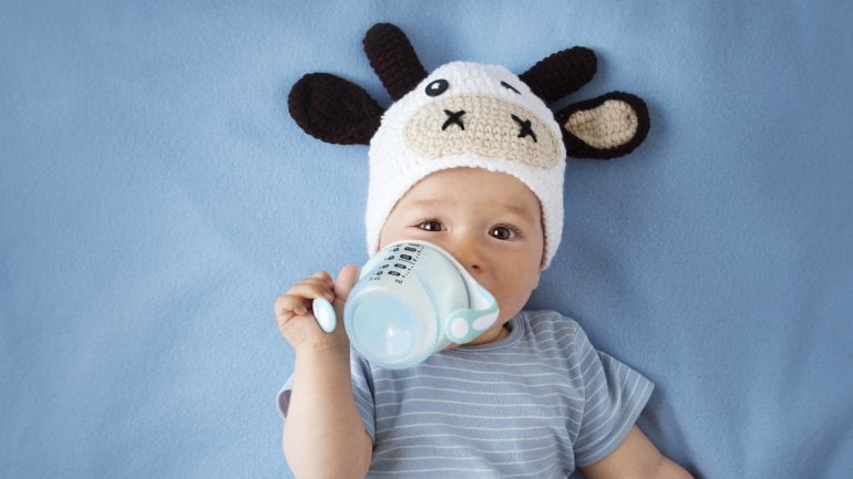 Ein Baby mit einer Kuhmütze trinkt aus einem Becher Milch.