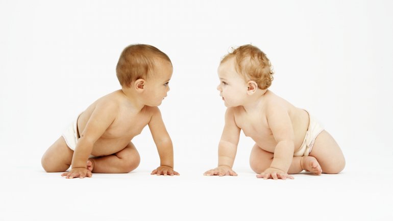 Auf dem Bild sind zwei Babies in Windeln, die sich ansehen.