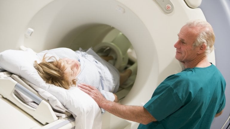 Das Bild zeigt wie eine Patientin von einem Pfleger ins MRT geschoben wird.