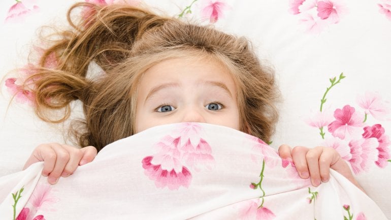 Das Bild zeigt ein Mädchen im Bett, das sich erschreckt.
