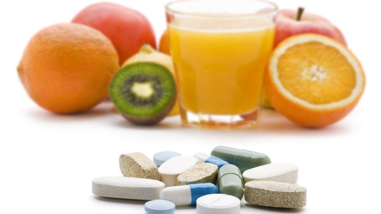 Man im Hintergrund Obst und ein Glas Orangensaft, im Vordergrund liegen verschiedene Tabletten.