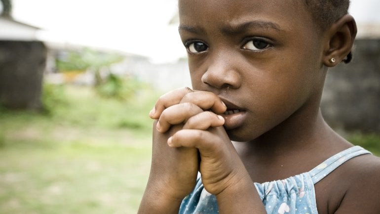 Ein afrikanisches Mädchen mit traurigem Gesichtsausdruck hält ihre gefalteten Hände vor ihren Mund.