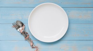 Nulldiät, weißer Teller auf blauem Tisch, Besteck mit Maßband