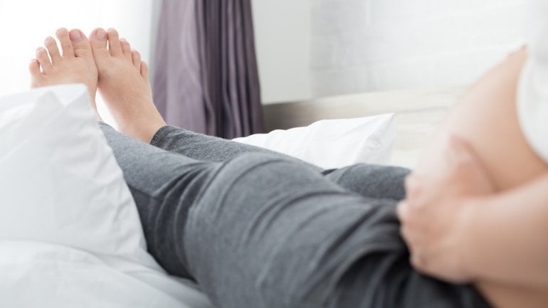 Eine schwangere Frau hat ihre Beine auf einem Bett hochgelegt.