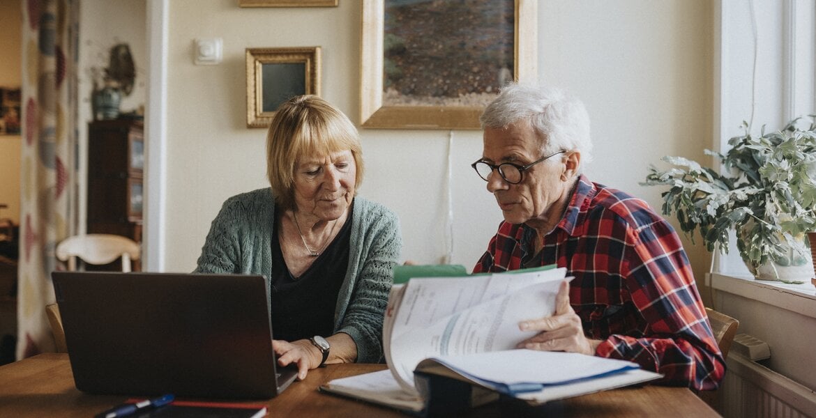 Patientenverfügung: Ein älterer Paar schaut Unterlagen durch und arbeitet am Laptop