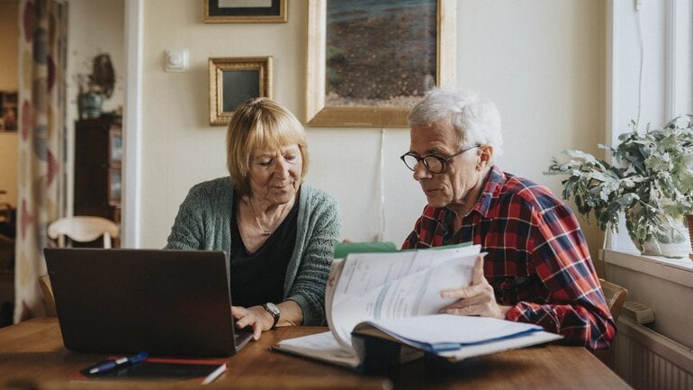 Patientenverfügung: Ein älterer Paar schaut Unterlagen durch und arbeitet am Laptop