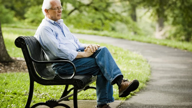 Ein älterer Mann sitzt auf einer Parkbank.