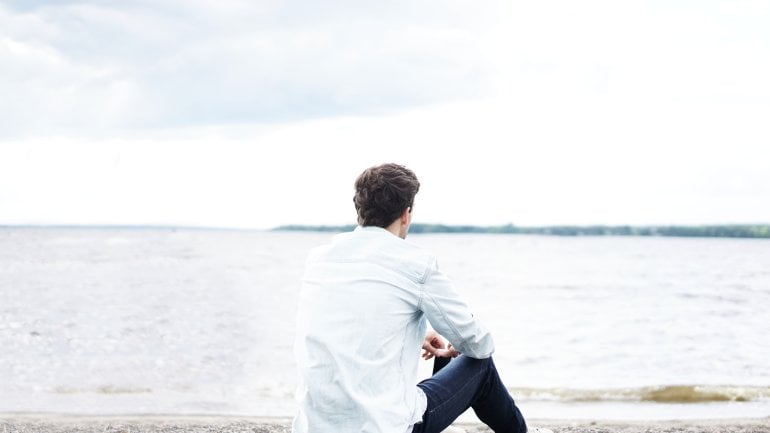 Das Bild zeigt einen jungen Mann, der an einem See sitzt.