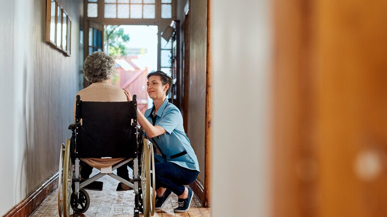 Pflegerin und Seniorin mit Rollstuhl im Heim