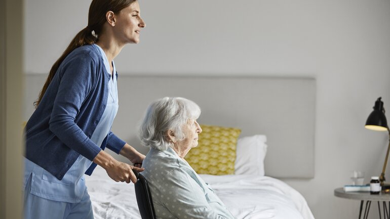 Verhinderungspflege Pflegerin schiebt alte Frau im Rollstuhl.jpg