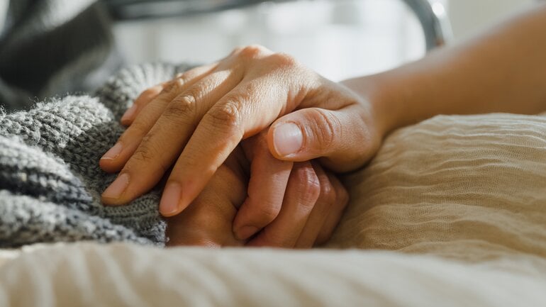 Mensch streichelt Hand einer schwerkranken Person