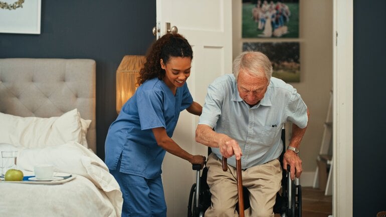 Pflegerin hilft Mann in den Rollstuhl