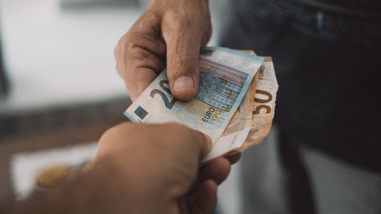 Hand eines älteren Menschen überreicht Geld an andere Person