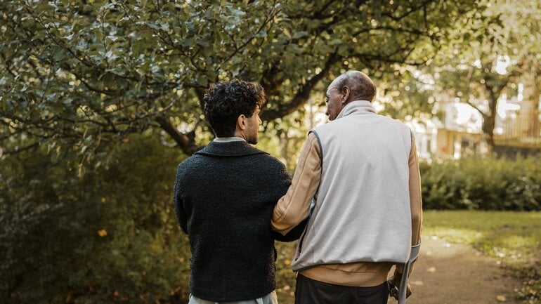 Junger Mann stützt Älteren mit Krücke beim Spazieren
