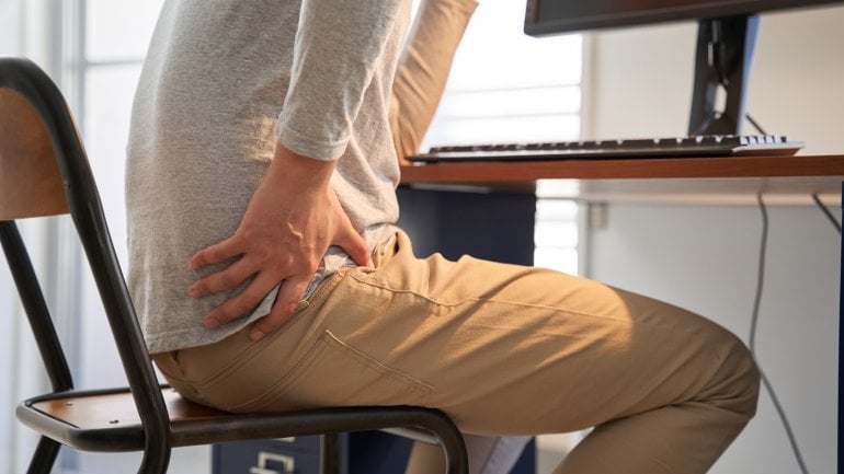 Piriformis-Syndrom: Mann sitzt am Schreibtisch und hat Schmerzen im Gesäß