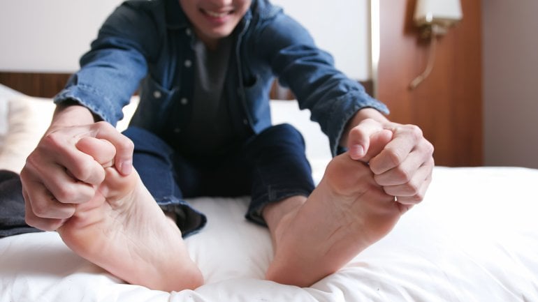 Polyneuropathie: Mann sitzt im Bett und fasst sich an schmerzende Füße.