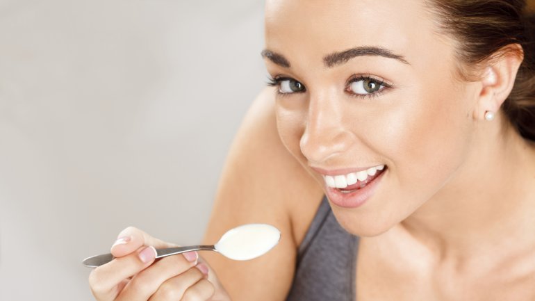 Das Bild zeigt eine junge Frau, die einen Löffel Joghurt isst.