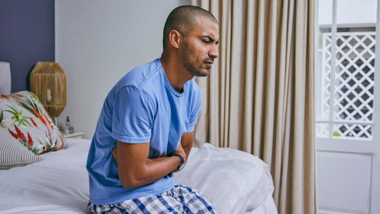Junger Mann mit Prostataentzündung sitzt auf Bett und hat Schmerzen.