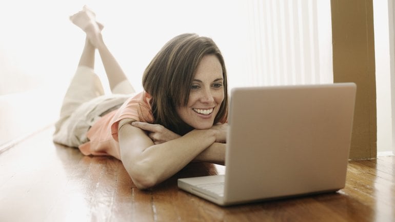 Eine Frau liegt auf dem Bauch und schaut auf einen Laptop.