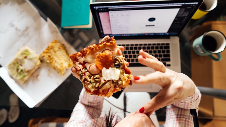 Eine Frau isst Pizza vor dem Laptop