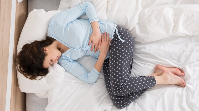 Eine Frau liegt mit Bauchschmerzen im Bett