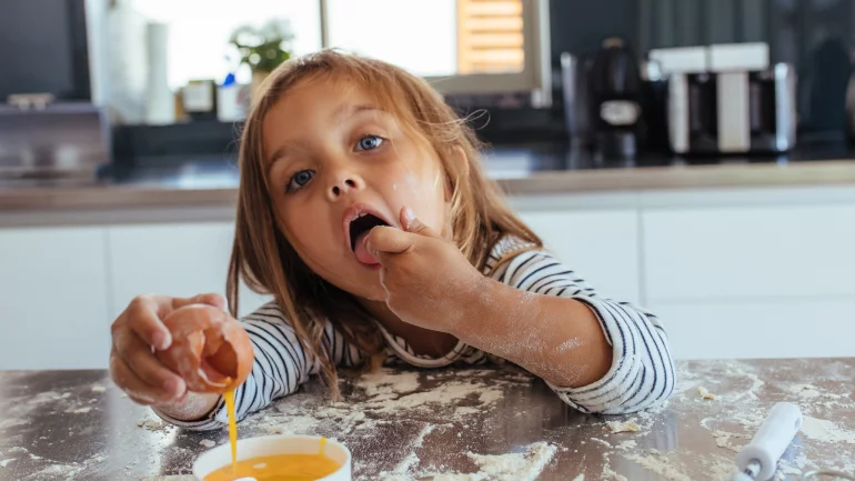 Salmonellen: Ein Kind hält ein aufgeschlagenes rohes Ei in der Hand und steckt sich einen Finger in den Mund.
